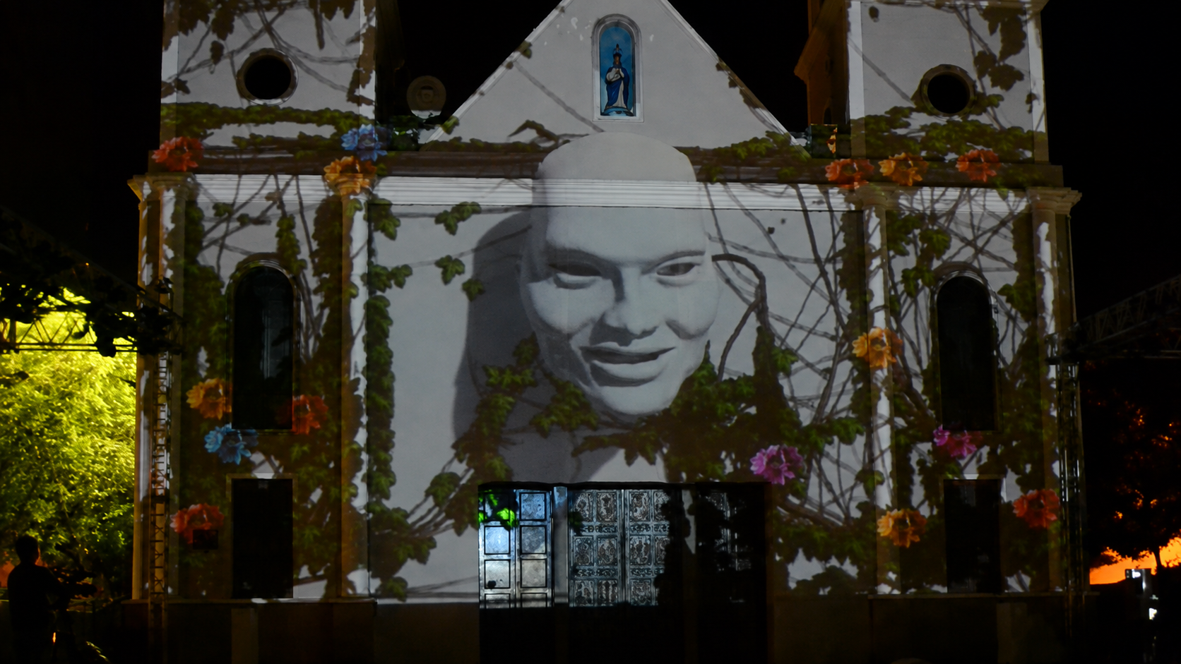 Retrato em preto e branco projetado sobre fachada, entre ramos e flores em cores