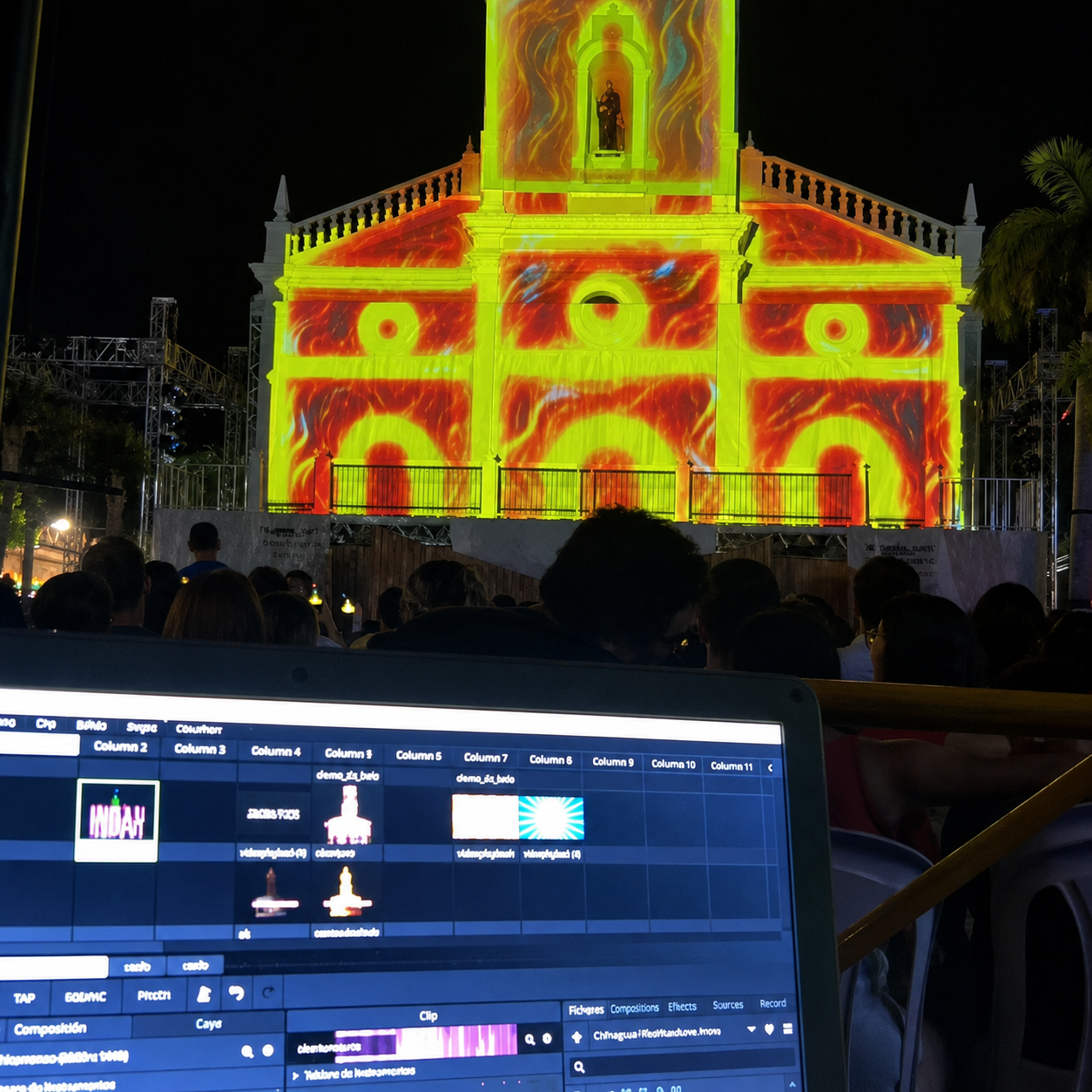Computador de operação audiovisual em primeiro plano diante do público e de uma fachada com projeção em vermelho e amarelo
